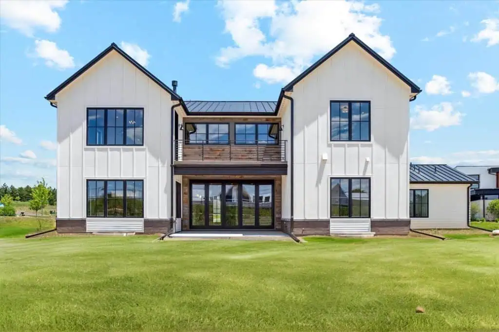 Modern farmhouse with green lawn and blue sky.