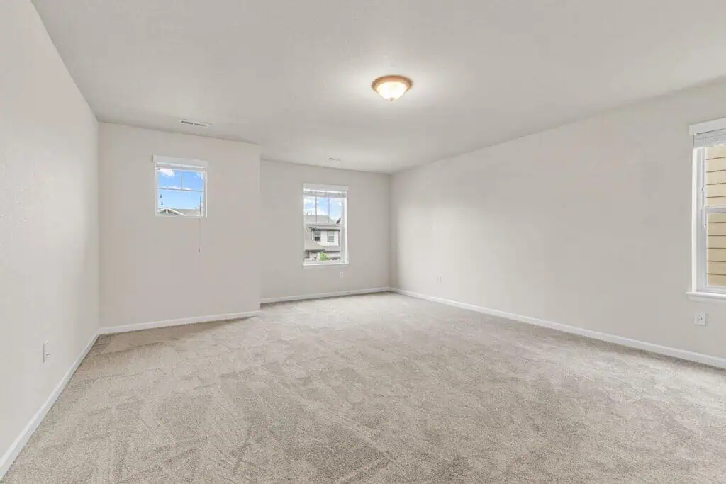 Spacious empty carpeted room with windows and light fixture.